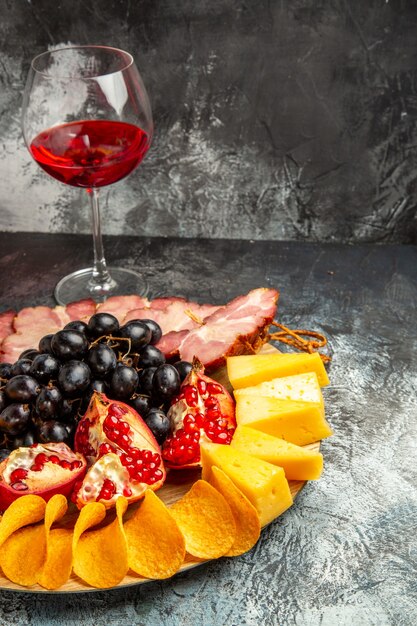 Bottom view cheese pieces meat grapes and pomegranate on oval serving board glass of wine on dark background