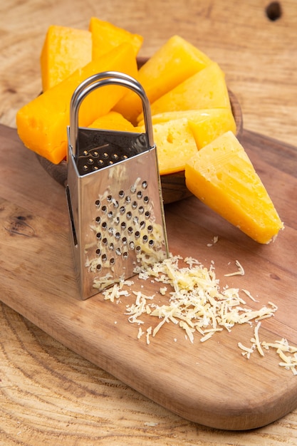 Bottom view cheese slices in wooden bowl box grater on cutting board on wooden surface