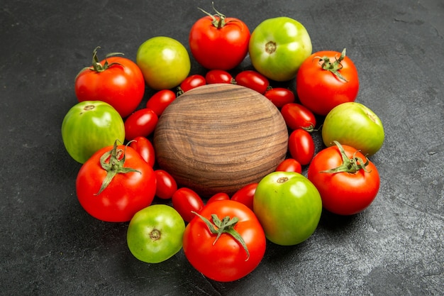 Вид снизу вишнево-красные и зеленые помидоры вокруг деревянной тарелки на темной земле