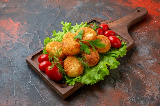 Free photo bottom view chicken nuggets lettuce cherry tomatoes on cutting board on dark table with copy space