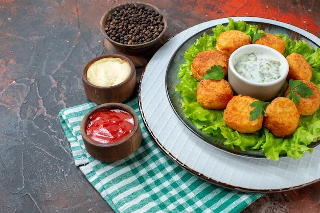 Foto gratuita pepite di pollo vista dal basso lattuga e salsa su piatto pepe nero in ciotola salse in piccole ciotole sul tavolo scuro