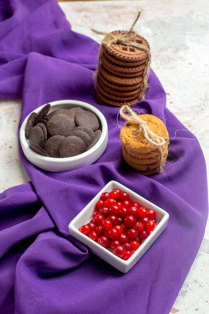 Vista dal basso cioccolato e frutti di bosco in ciotole biscotti a scialle viola legati con una corda sul tavolo bianco