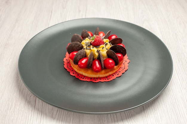 Bottom view chocolate cake rounded with cornel and raspberry in the center in the grey plate on the white wooden background