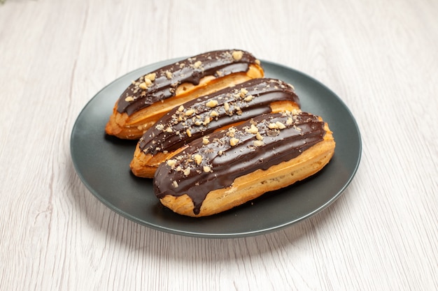 Free photo bottom view chocolate eclairs on the grey plate on the white wooden background