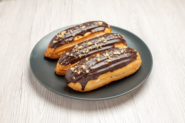 Bottom view chocolate eclairs on the grey plate on the white wooden background