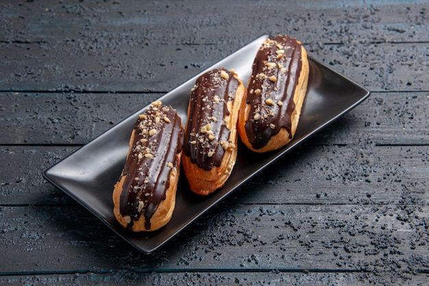 Bottom view chocolate eclairs on rectangle plate on the dark wooden table with free space