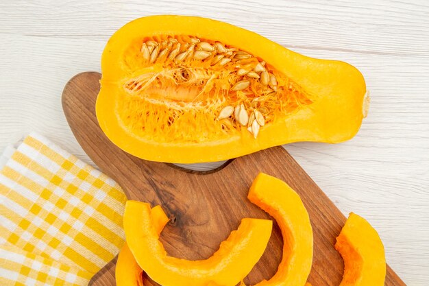 Bottom view chopped butternut squash on chopping board squash cut in half yellow white checkered kitchen towel on grey table