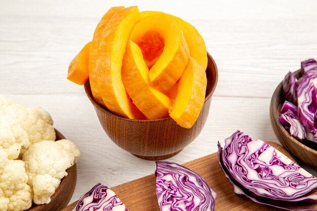 Bottom view chopped pumpkin cauliflower cut red cabbage on board in bowls on white surface