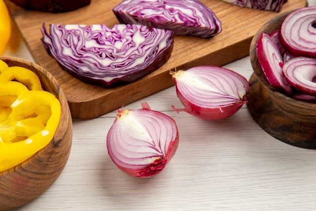 Bottom view chopped red cabbages cut onion cut bell peppers in bowls on white surface