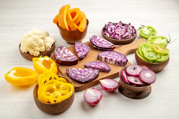 Bottom view chopped red cabbages on cutting board cut bell peppers cut pumpkin cut onion in bowls on white surface