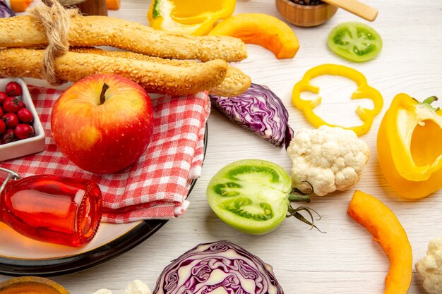 Bottom view chopped vegetables apple bread red bottle on napkin on round plate on white table