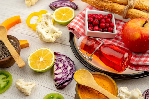 Bottom view chopped vegetables apple bread red bottle on napkin on round platter various spices in small bowls on table