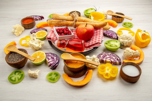 Bottom view chopped vegetables apple bread red bottle on napkin on white platter various spices in small bowls on table