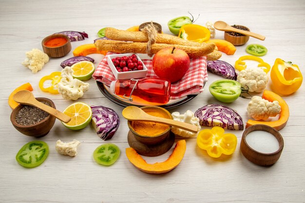 Bottom view chopped vegetables apple bread red bottle on napkin on white platter various spices in small bowls on table