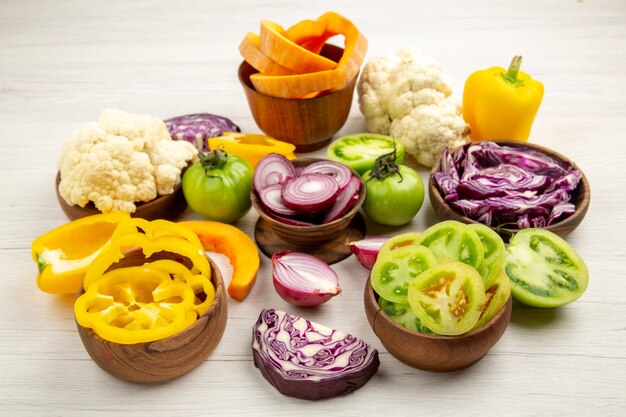 Bottom view chopped vegetables bell peppers green tomatoes red cabbages onions cauliflower pumpkins in bowls on white wooden table