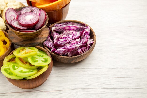 Bottom view chopped vegetables cut red cabbage cut pumpkin cut onion cut green tomatoes in bowls on white table with copy place