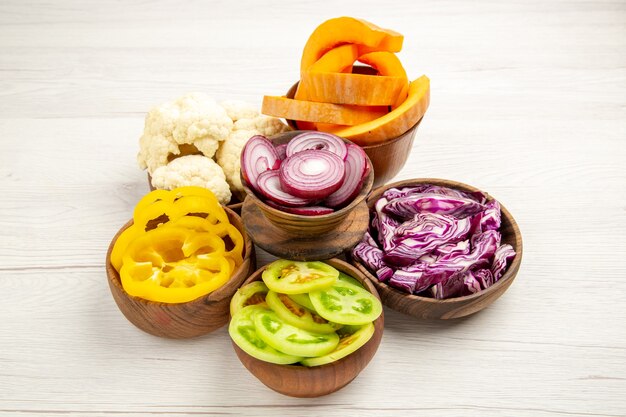 Bottom view chopped vegetables cut red cabbage cut pumpkin cut yellow bell peppers cut onion cut green tomatoes cauliflower in bowls on wooden surface