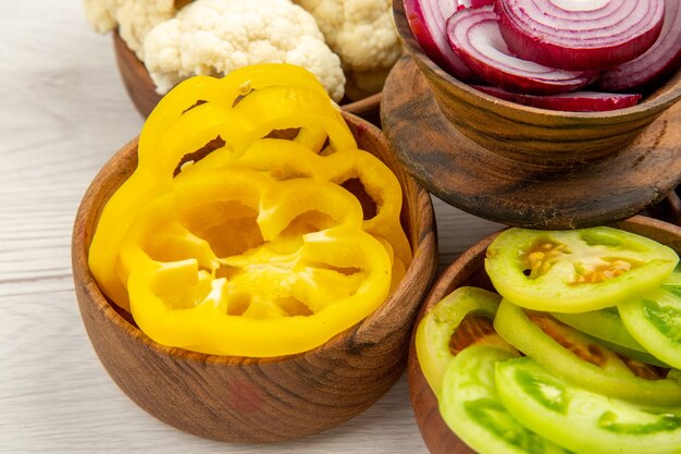 Bottom view chopped vegetables cut yellow bell peppers cut onion cut green tomatoes cauliflower in bowls on white table