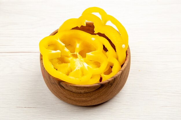 Bottom view chopped yellow bell peppers in wooden bowl on white table