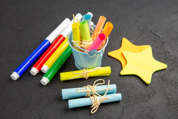 Bottom view colored markers rolled up sticky notes tied with rope in small bucket star sticky notes on black table