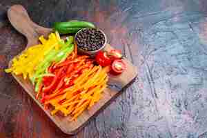 Free photo bottom view colorful cut peppers black pepper tomatoes cucumber on choppingboard on dark red table with copy space