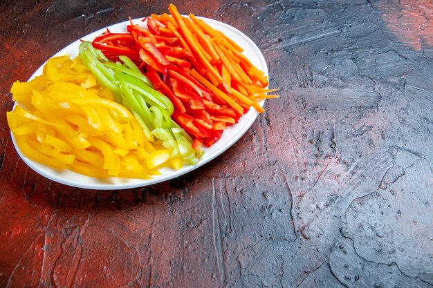 Bottom view colorful cut peppers on white plate on dark red table free space