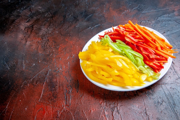 Bottom view colorful cut peppers on white plate on dark red table with free space