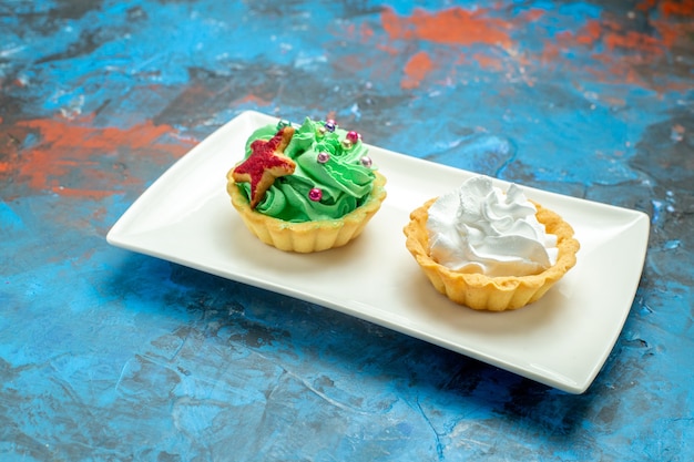 Bottom view cream tarts on white rectangular plate on blue red surface