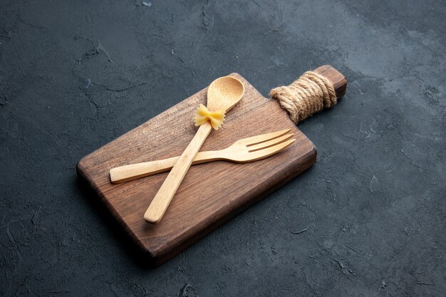 Bottom view crossed wooden spoon and fork on wooden serving board on dark surface with copy place