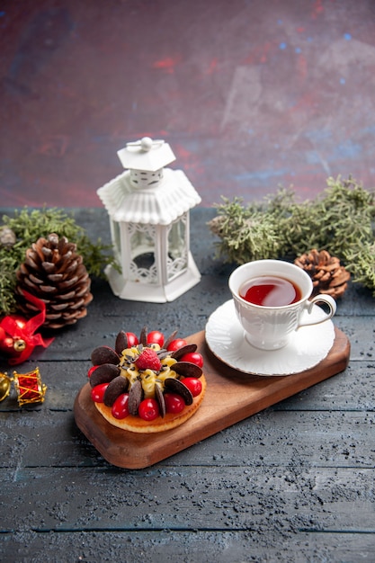 Bottom view a cup of tea and berry cake on wooden serving plate pinecones christmas toys and white lantern on dark wooden table