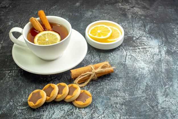 Bottom view cup of tea flavored by lemon and cinnamon lemon slices in small saucer biscuits tied cinnamon sticks on dark table free space