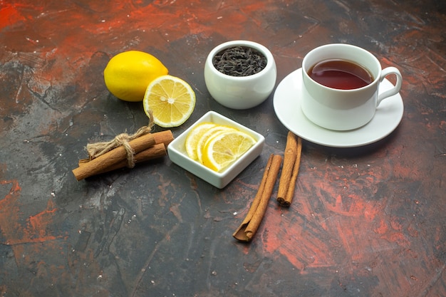 Free photo bottom view cup of tea lemon slices in bowl cinnamon sticks tea in bowl on dark red background