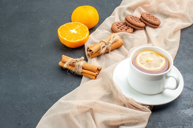 Bottom view a cup of tea with lemon cinnamon sticks cookies on beige shawl orange on dark surface