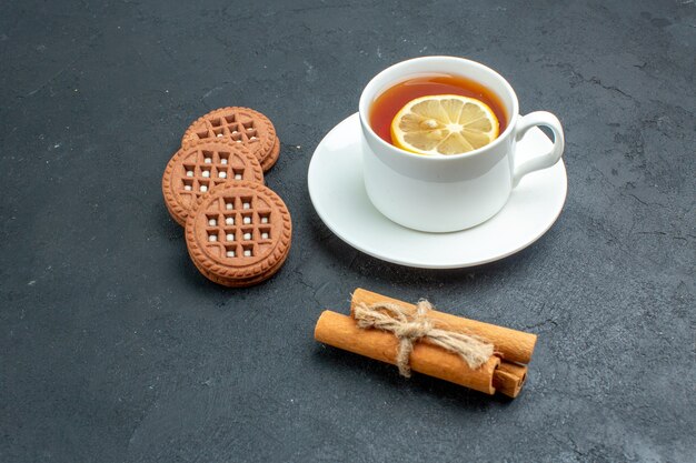 Вид снизу чашка чая с печеньем в палочках с лимоном и корицей на темной поверхности