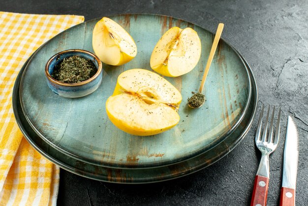 Вид снизу нарезанные яблоки сушеная мята в миске деревянной ложкой на тарелке, ножом и вилкой желтое кухонное полотенце на темной земле