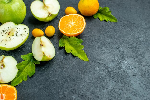 Bottom view cut apples and mandarines cumcuat leaves on dark table free space