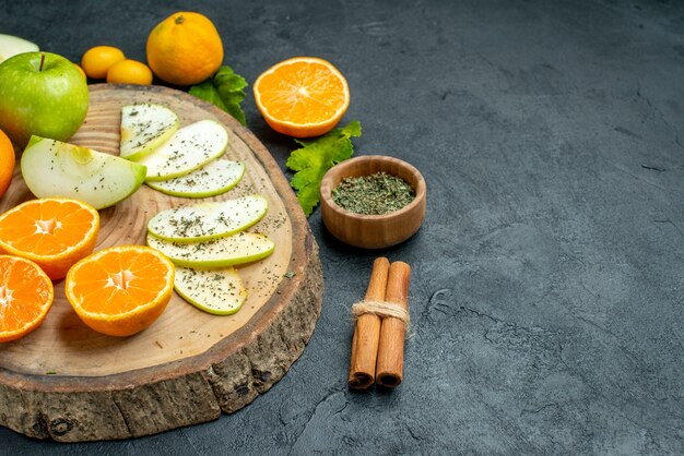 Bottom view cut apples and mandarines on rustic serving board tied cinnamon sticks dried mint powder bowl cumcuat on dark table copy place