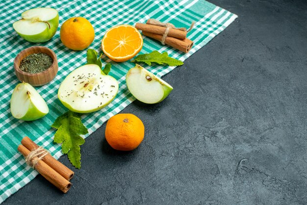 Bottom view cut apples and tangerines cinnamon sticks dried mint powder in bowl on green tablecloth on dark table copy space