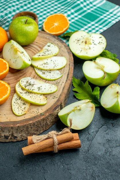 Free photo bottom view cut apples and tangerines on wood board cinnamon on green tablecloth on dark table