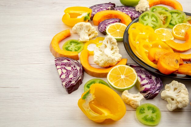 Bottom view cut vegetables and fruits pumpkin bell peppers persimmon red cabbage green tomatoes on black plate on wooden table