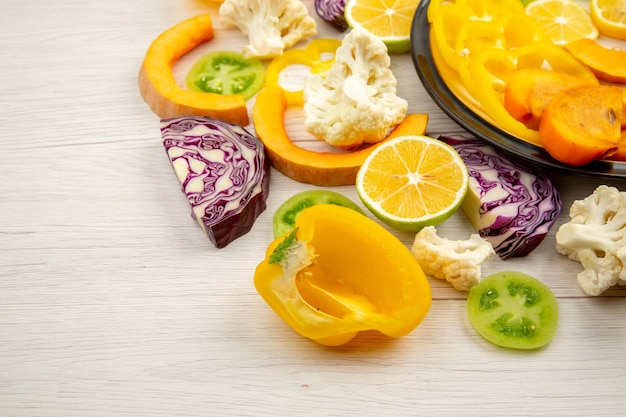 Bottom view cut vegetables and fruits pumpkin bell peppers persimmon red cabbage green tomatoes on plate on wooden table