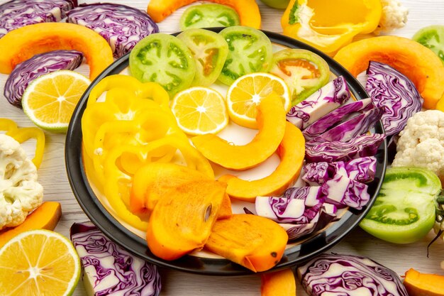 Bottom view cut vegetables and fruits yellow bell peppers pumpkin persimmon red cabbage lemon green tomatoes on platter on table