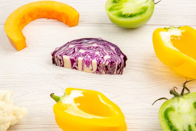 Bottom view cut vegetables red cabbage green tomato pumpkin yellow bell pepper on white wooden surface
