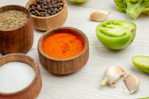 Free photo bottom view different spices in small bowls cut green tomatoes garlic on white table