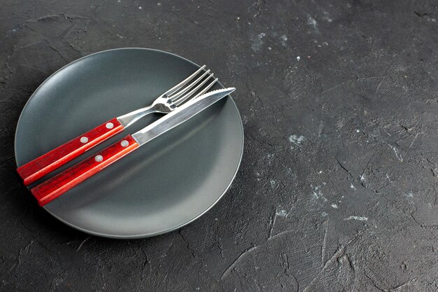 Bottom view a fork and knife on black round platter on dark surface free space