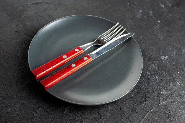 Bottom view a fork and knife on black round platter on dark surface