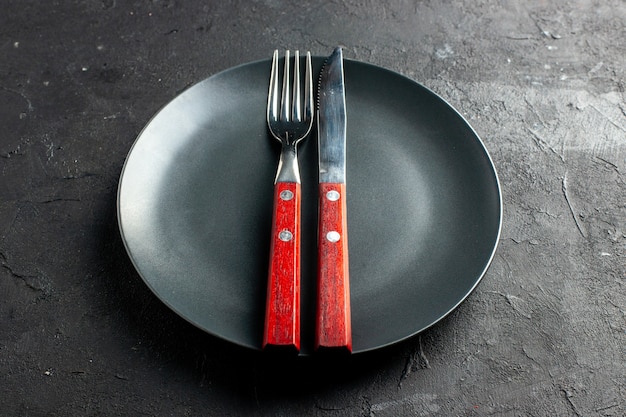 Bottom view a fork and knife on black round platter on dark table