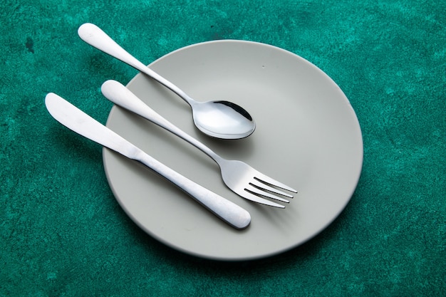 Free photo bottom view fork spoon knife on plate on green surface