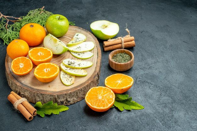 Bottom view fresh apple and orange slices on wood board dried mint powder in bowl cinnamon sticks pine tree branches on black table free space