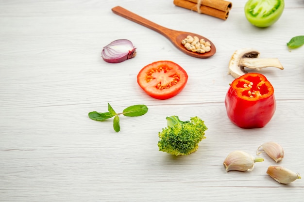 Bottom view fresh cut vegetables wooden spoon mushrooms green and red tomato onion broccoli garlic on grey table free place